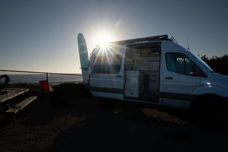 RV rental camper van with surfboard, parked beachside as the sun sets. Interior visible, ideal for surf and adventure travel.