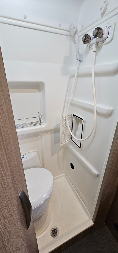 Inside an RV rental: a compact white wet bath featuring a toilet, handheld shower, and recessed storage, designed for efficiency.
