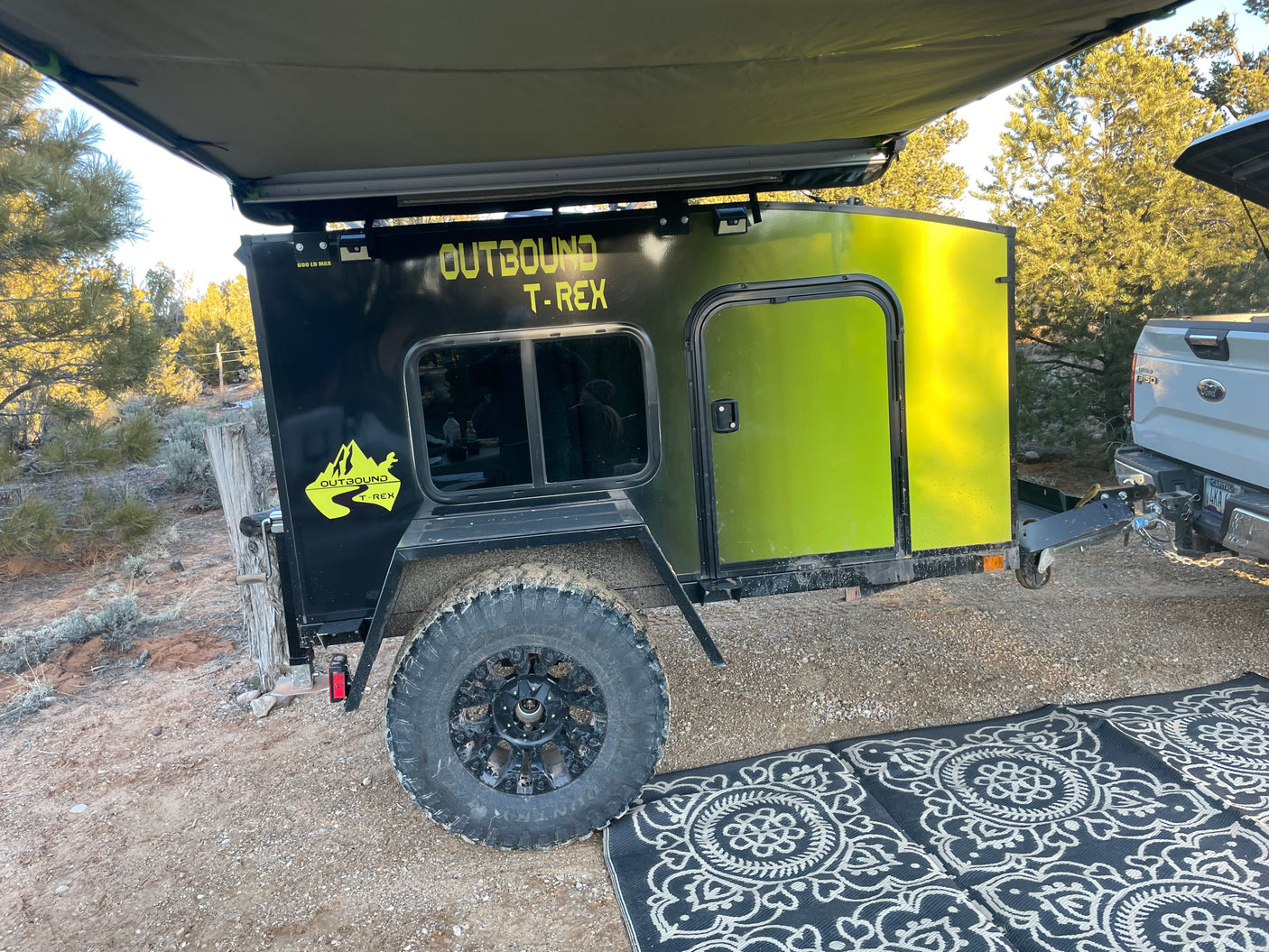 This Outbound T-Rex off-road teardrop trailer, ideal for rv rental adventures, is set up for camping with an awning & rug.