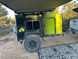 This Outbound T-Rex off-road teardrop trailer, ideal for rv rental adventures, is set up for camping with an awning & rug.