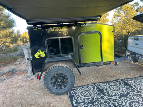 This Outbound T-Rex off-road teardrop trailer, ideal for rv rental adventures, is set up for camping with an awning & rug.