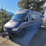 Gray camper van (RV rental) idles in nature. Mountains, lake, bird & exhaust visible. Perfect for road trips!
