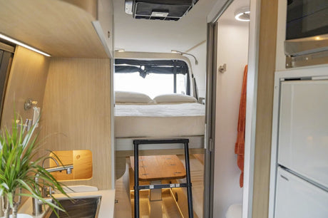 Modern RV rental interior with elevated bed, kitchenette, and compact bathroom. Perfect for motorhome adventures.