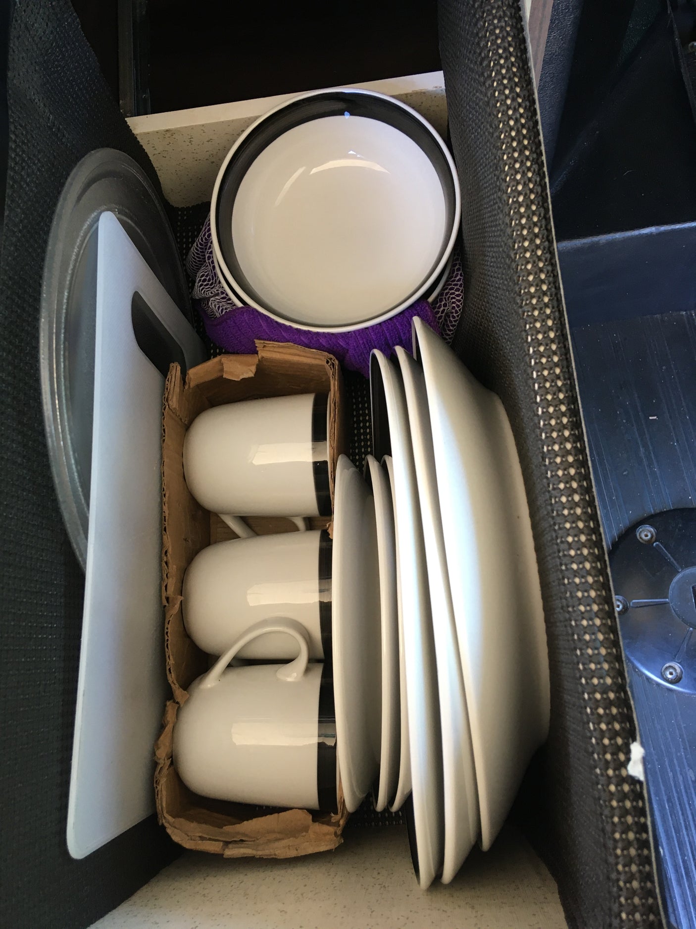 RV rental kitchen setup: white dishes, bowls, cups in a caddy, and a cutting board, compactly organized for travel.