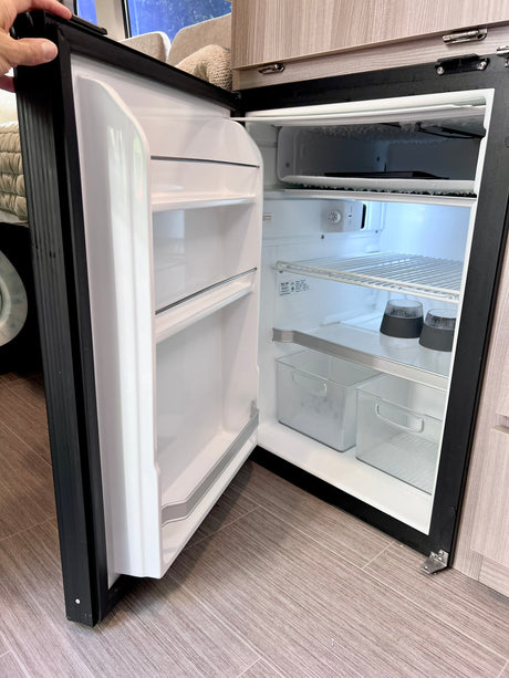 An open refrigerator inside an RV rental. Note the frosty freezer, shelves, bins, and cups, essential for your travels.