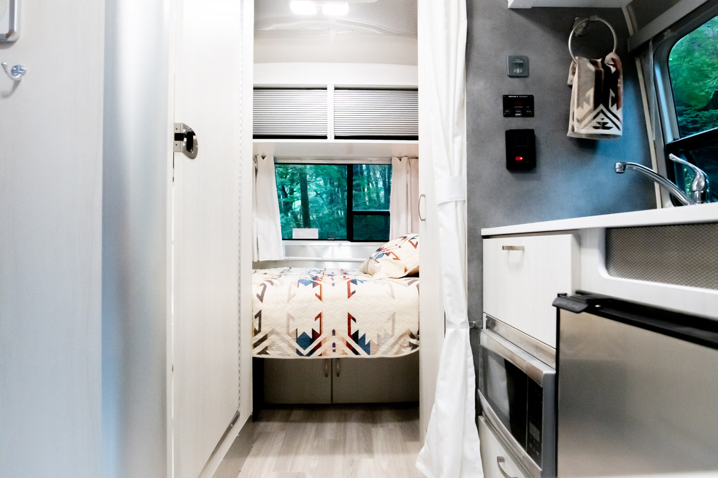 Bright, cozy rv rental interior. Comfortable bed with forest views, plus a compact kitchen. Ideal for your next road trip.