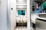 Bright, cozy rv rental interior. Comfortable bed with forest views, plus a compact kitchen. Ideal for your next road trip.