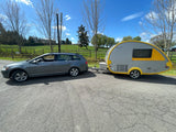 Grey VW station wagon towing a yellow/grey teardrop camper on an asphalt road. Perfect RV rental for your next adventure.