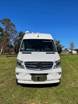 This white Mercedes Sprinter camper van, perfect for an rv rental, is parked on green grass with trees under a blue sky.
