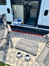 RV rental's outdoor living: pet bed, bowls, pull-out table, and rug create a cozy camp setup outside the van.