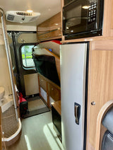 Compact RV rental interior featuring kitchen, folded bed area, and small bathroom for mobile living adventures.