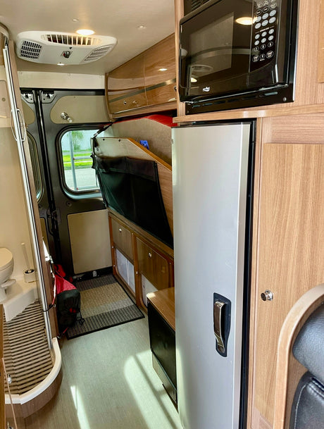 Compact RV rental interior featuring kitchen, folded bed area, and small bathroom for mobile living adventures.