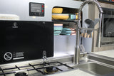 Compact RV rental kitchen with Dometic stove, sink, colorful dishes, and an InTech control panel for water and power.