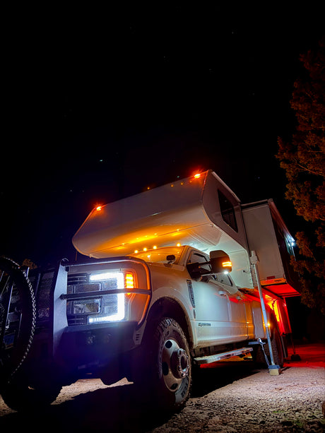 Nighttime view of a brightly lit heavy-duty truck camper, an ideal RV rental for rugged adventures under a starry sky.