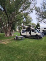 Scenic rv rental setup: custom camper van with pop-top tent at a lush green campsite with picnic table.