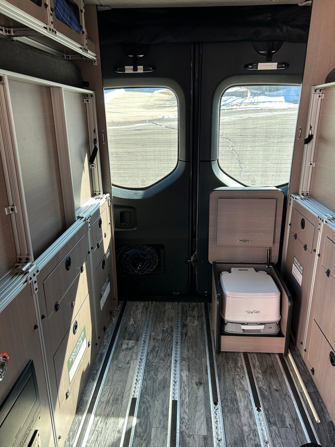 Inside this RV rental, modular storage, L-track floor, and a hidden portable toilet create a compact camper van setup.