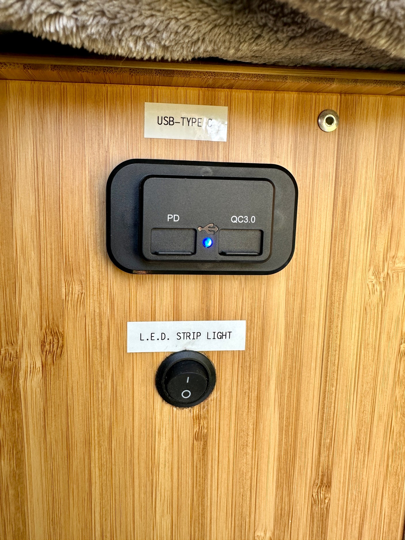 RV rental charging panel: USB-C PD/QC3.0 ports (blue light on) and LED strip light switch on wood.