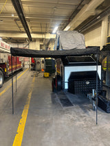 Off-road camping trailer for rv rental, featuring an extended awning, rooftop tent, and solar panels, parked in a large garage.