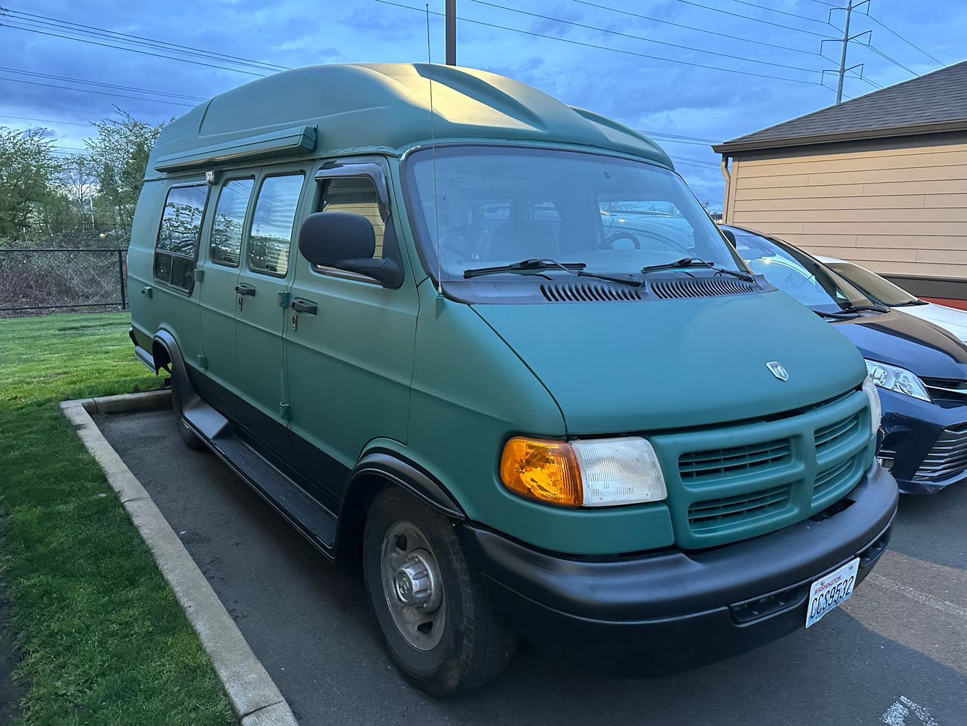 A distinctive green high-top van, ideal for RV rental adventures, parked on asphalt near grass under a cloudy sky.
