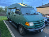 A distinctive green high-top van, ideal for RV rental adventures, parked on asphalt near grass under a cloudy sky.