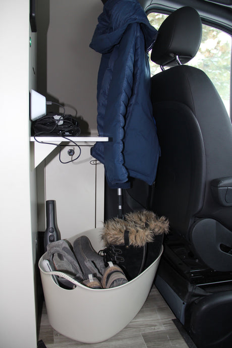 RV rental: Organized camper van interior with blue jacket, charging station, and shoe storage in a bin.