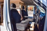 RV rental interior showing front black seats, dashboard, and a view out to a road with autumn trees.