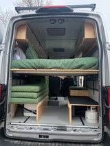 Inside an RV rental, a custom camper van layout features a convertible bed, integrated storage, and cooking essentials.