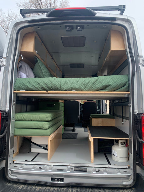 Inside an RV rental, a custom camper van layout features a convertible bed, integrated storage, and cooking essentials.