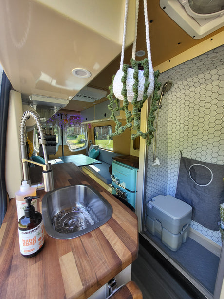 RV rental interior showcases a compact kitchen, hexagon-tiled shower, and portable toilet setup.