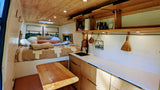 Inside a spacious RV rental: a cozy bedroom, well-equipped kitchen with sink, fold-down table, & ample storage.