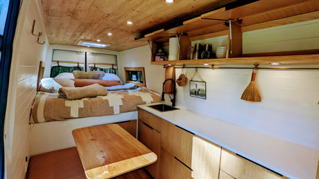 Inside a spacious RV rental: a cozy bedroom, well-equipped kitchen with sink, fold-down table, & ample storage.