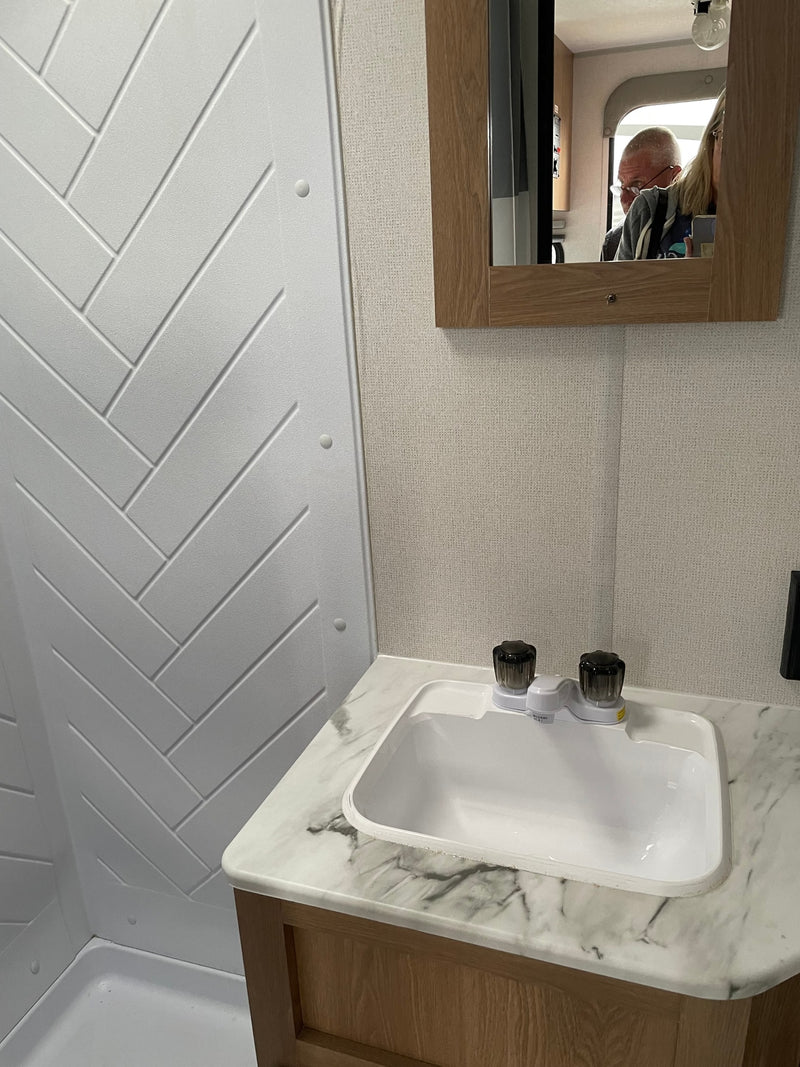 RV rental bathroom: compact vanity with sink & herringbone shower. Mirror reflects occupant. — photo 4