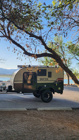 This Drifter RV rental camper is perfectly parked lakeside, under trees with mountains, ready for your next outdoor adventure.