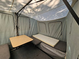 Inside an RV rental camper: light grey canvas interior with a wooden table, grey cushions, and a foam mattress.