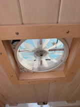 Inside an RV rental, a ceiling fan/vent with a mesh screen is framed by light wood panels, showing the sky above.