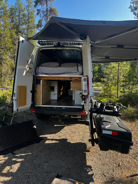 This RV rental camper van reveals its custom interior, comfy bed, and outdoor setup with awning, solar panel, and bike rack.