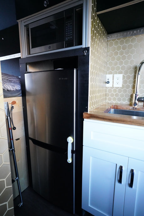 Compact RV rental kitchen features stainless fridge, overhead microwave, sink, wood counters, & hexagonal tile backsplash.