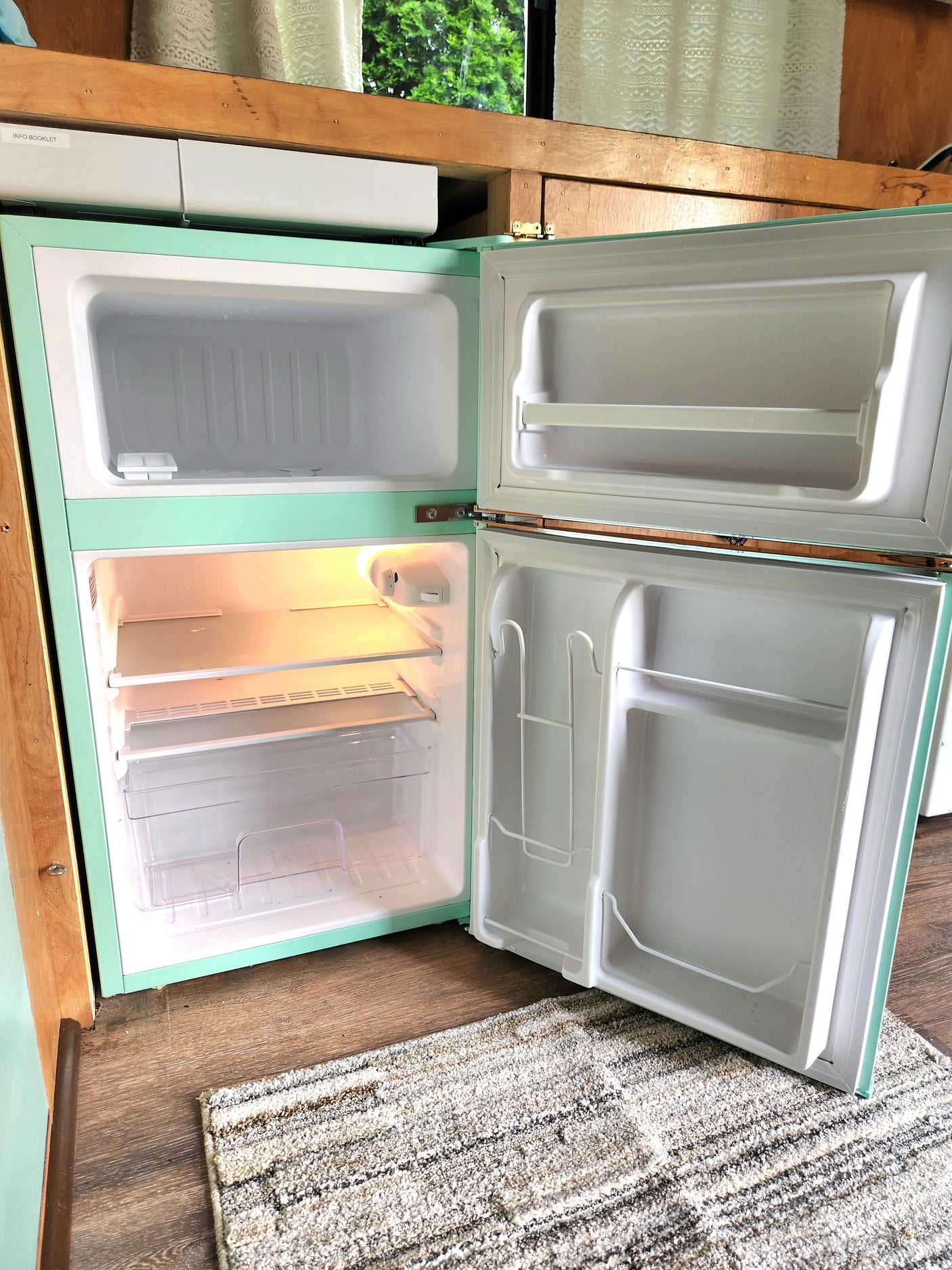 See inside this RV rental's retro mint green compact refrigerator. Both doors are open, revealing clean, empty compartments.