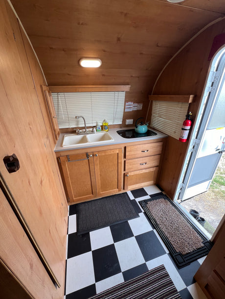 Compact RV rental kitchen interior featuring a sink, cooktop, wood cabinetry, and checkerboard floor. Essentials for your trip!
