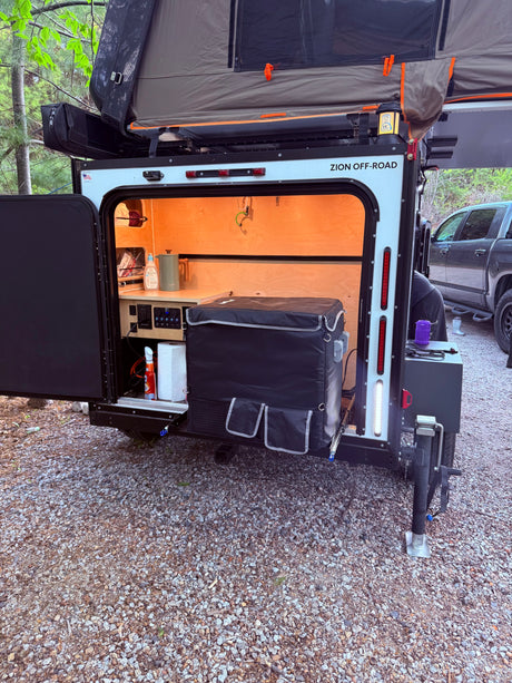 Zion Off-Road camper shows its open rear galley kitchen with fridge & controls, plus a rooftop tent. Great for an rv rental getaway.
