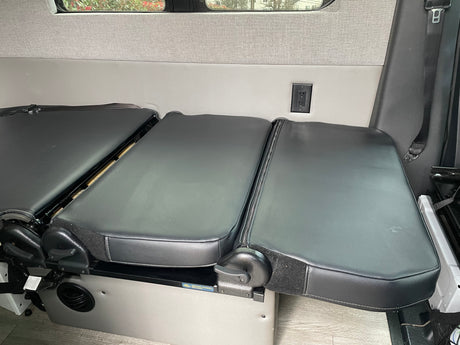 This RV rental interior features convertible black bench seats that fold out for flexible living space, equipped with a convenient power outlet.