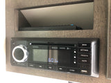 An RV rental's Jensen JWM70A stereo, displaying 6:01 PM, with a remote in a cubby above, is ready for entertainment.