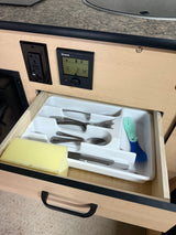 Open RV rental kitchen drawer: a cutlery organizer, sponge, & child's spork. A Truma control panel (E 2 H) & outlet are visible.