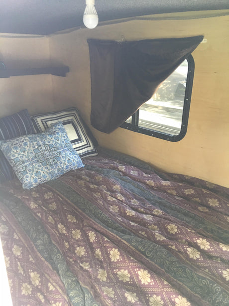Cozy RV rental camper interior: bed with patterned bedding, pillows, window, shelf. Ideal for travel.