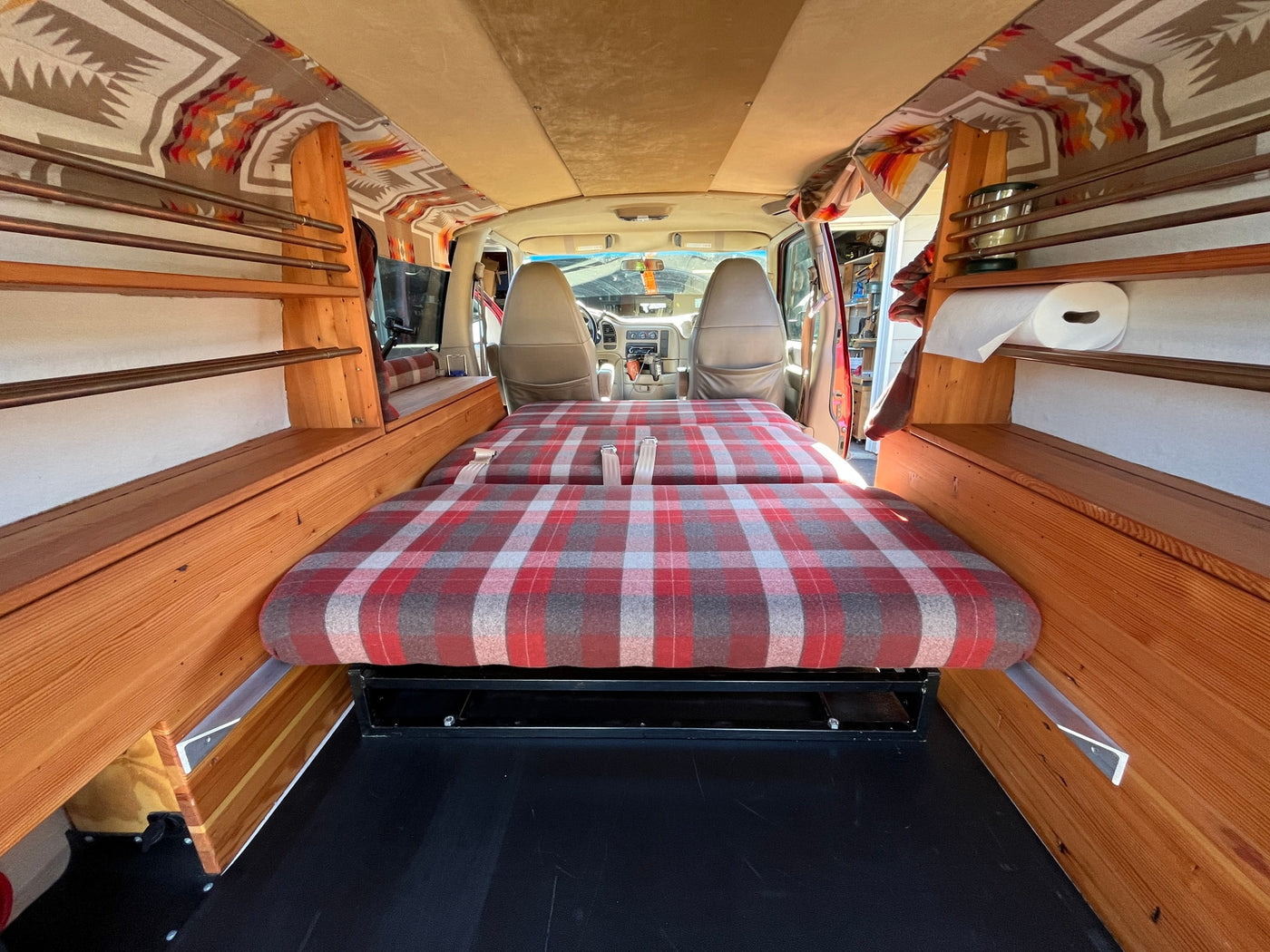 RV rental: Inside a converted camper van featuring a plaid bed, built-in wooden shelving, and patterned ceiling. — photo 8