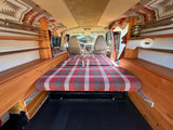 RV rental: Inside a converted camper van featuring a plaid bed, built-in wooden shelving, and patterned ceiling.