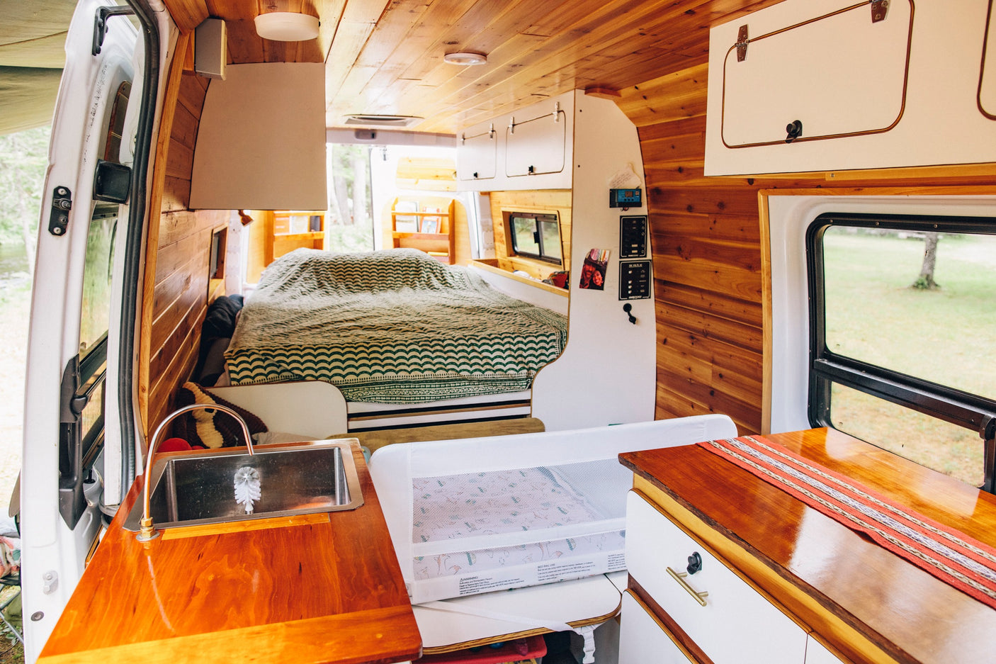Cozy RV rental camper van interior: wood-paneled, featuring a bed, kitchenette, and child rail for family travel.
