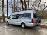 Silver Winnebago Boldt rv rental parked by a muddy river, ready for adventure with bikes on the back.