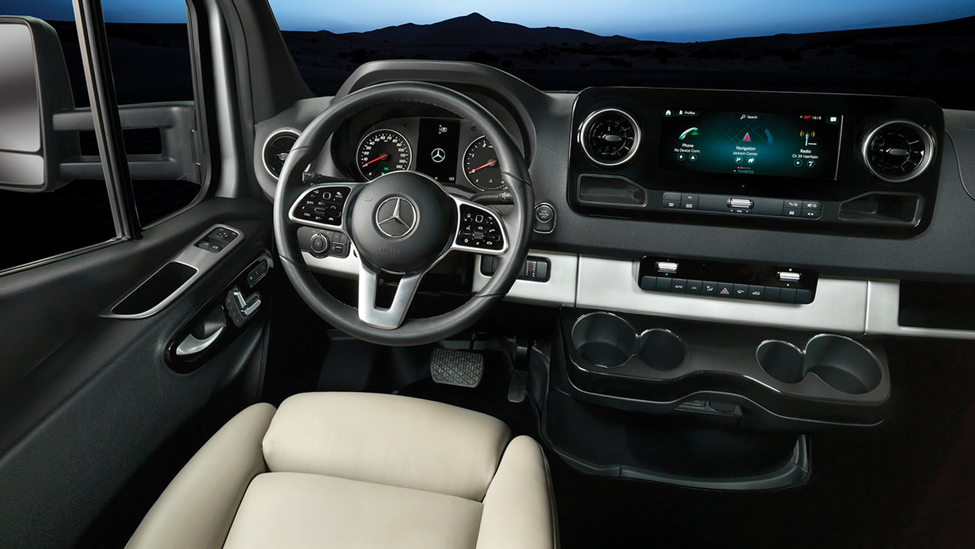 Inside a modern Mercedes-Benz Sprinter RV rental: driver's cockpit with navigation screen, steering wheel, and sleek controls.