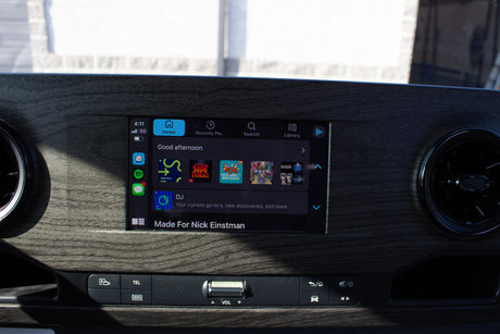 An RV rental's infotainment screen displays a personalized music player ("Made For Nick Einstman"), with physical media controls below.